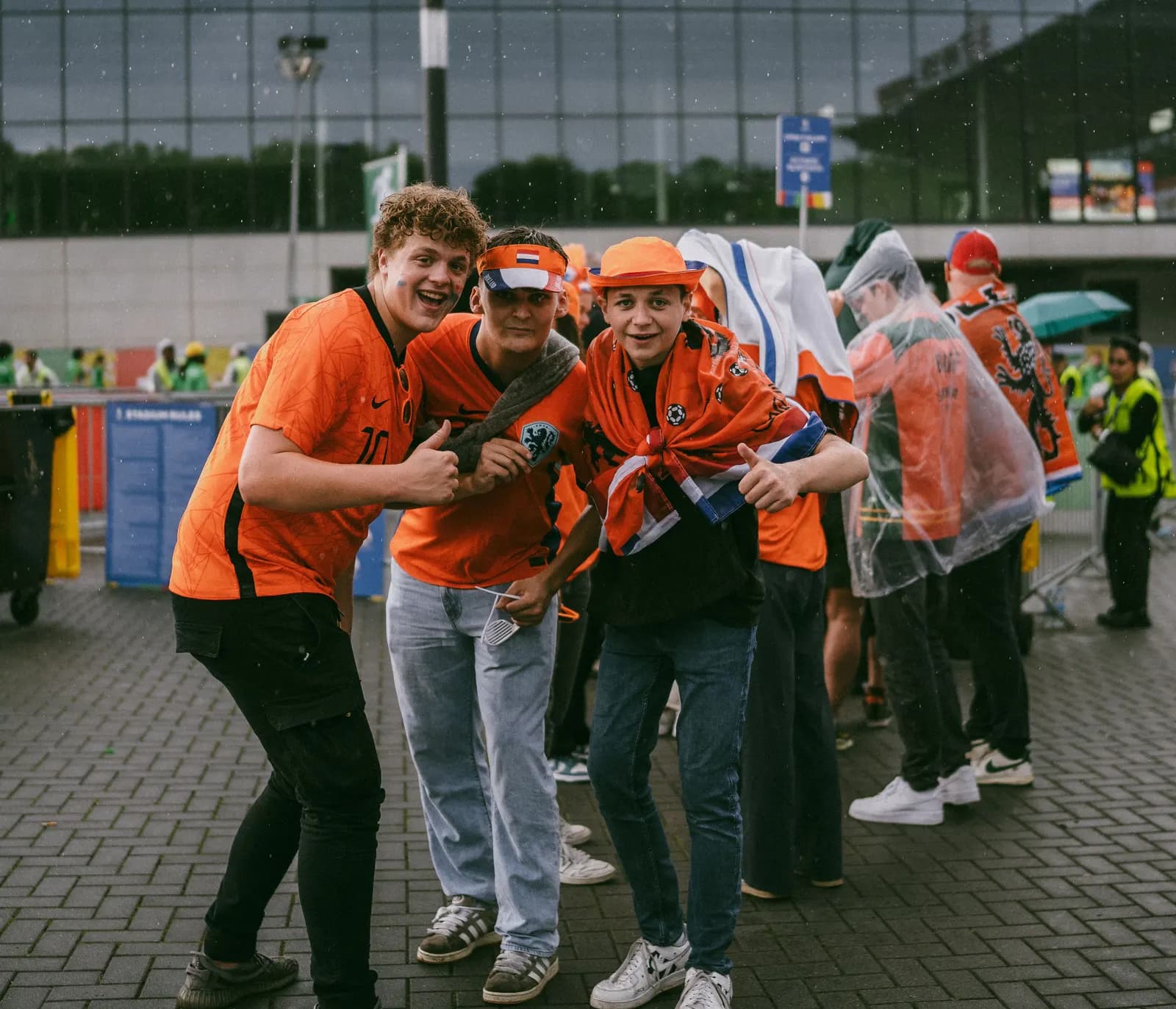 Football supporters in orange shirts posing together outside a stadium in the rain.